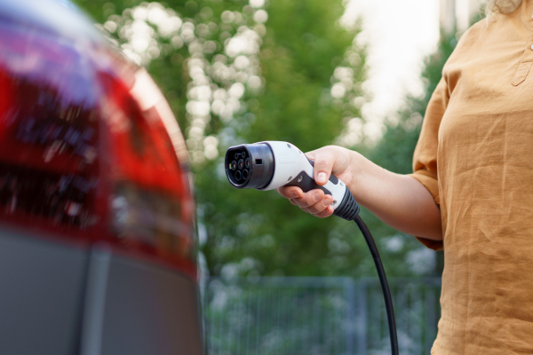 A woman holding power supply cable at electric vehicle charging station, closeup