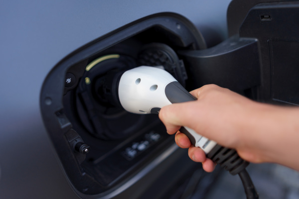 A man holding power supply cable at electric vehicle charging station, closeup