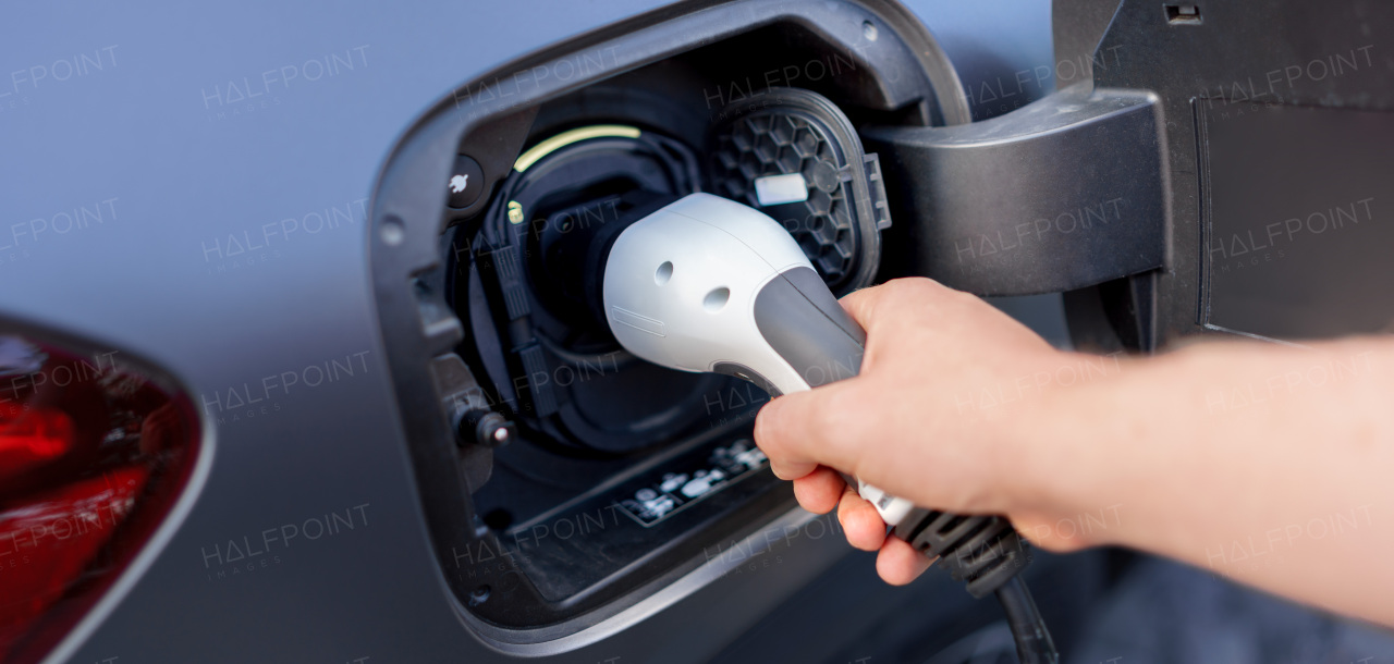 A man holding power supply cable at electric vehicle charging station, closeup