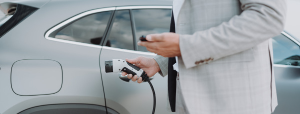 A man holding power supply cable at electric vehicle charging station, closeup