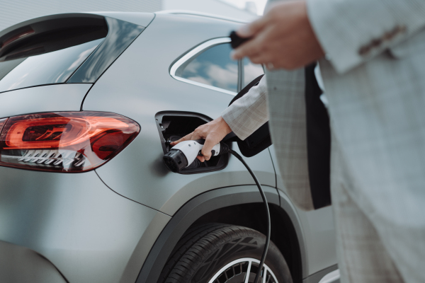 A man holding power supply cable at electric vehicle charging station, closeup