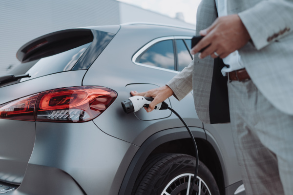 A man holding power supply cable at electric vehicle charging station, closeup