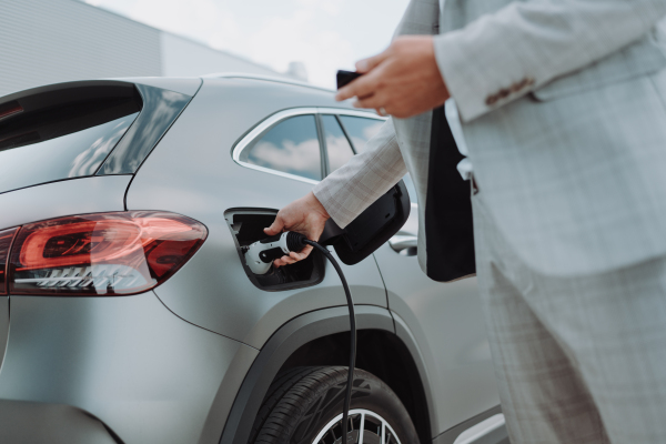 A man holding power supply cable at electric vehicle charging station, closeup