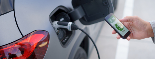 A man holding smartphone while charging car at electric vehicle charging station, closeup.