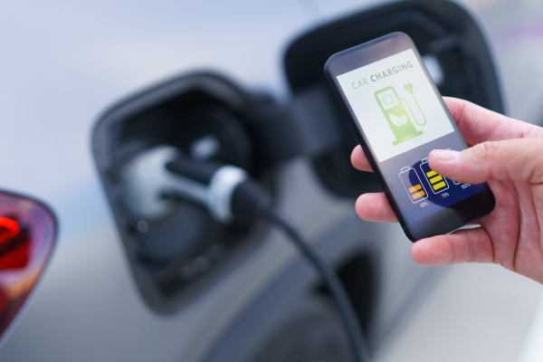 A man holding smartphone while charging car at electric vehicle charging station, closeup.