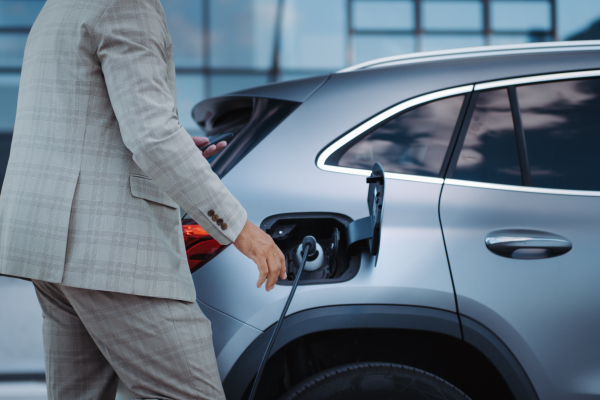 A man holding smartphone while charging car at electric vehicle charging station, closeup.