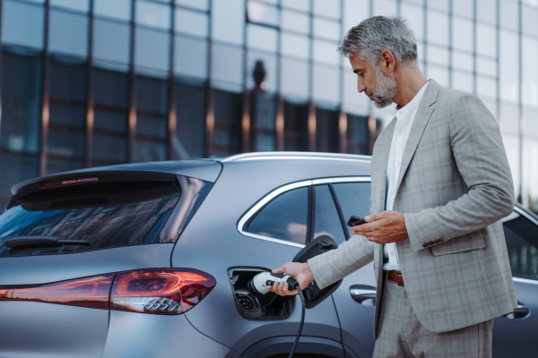 A man holding power supply cable at electric vehicle charging station, closeup