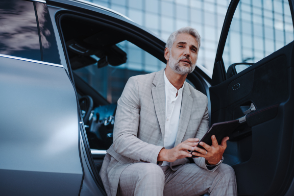 Businessman using tablet while charging a car at electric vehicle charging station, close-up.