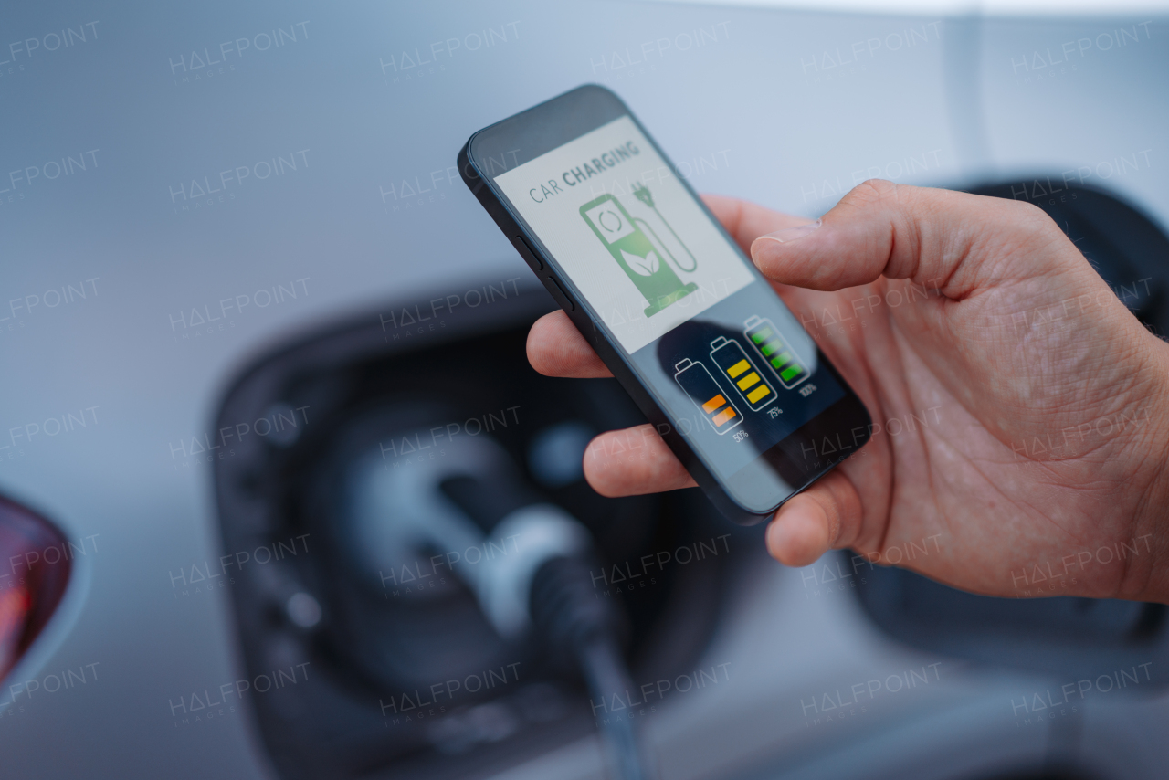 Man setting phone application for charging his electric car at a charging station, closeup.