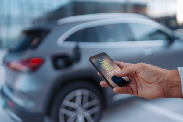 A man holding smartphone while charging car at electric vehicle charging station, closeup.