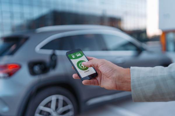 A man holding smartphone while charging car at electric vehicle charging station, closeup.