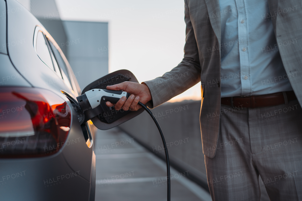 A man holding power supply cable at electric vehicle charging station, closeup