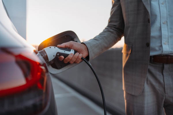 A man holding power supply cable at electric vehicle charging station, closeup