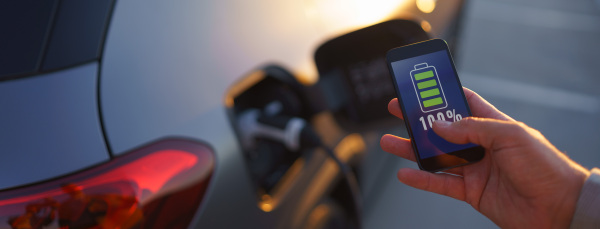 A man holding smartphone while charging car at electric vehicle charging station, closeup.