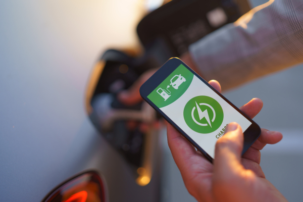 A man holding smartphone while charging car at electric vehicle charging station, closeup.