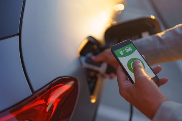 A man holding smartphone while charging car at electric vehicle charging station, closeup.