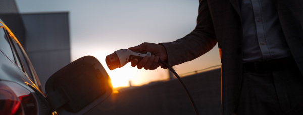 A man holding power supply cable at electric vehicle charging station, closeup