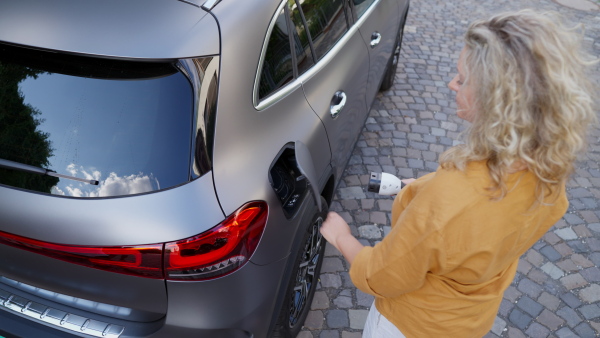 Woman charging battery of electric car in driveway. Top shot.