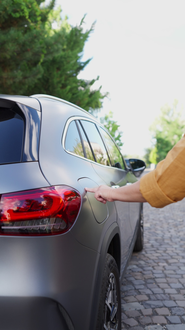 Woman charging battery of electric car in driveway. Vertical shot.