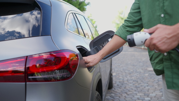 Close up of man charging electric car in driveway.