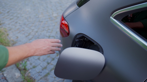 Close up of man charging battery of electric car in driveway. Top shot.