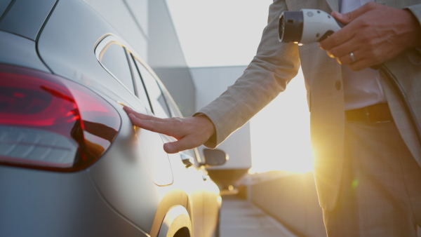 Close up of businessman charging electric car with sunset background.