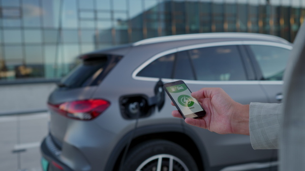 Man looking at smart phone app while charging electric car battery.