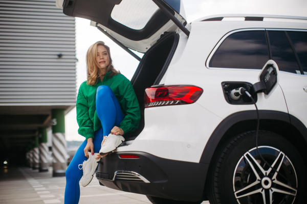 Young woman in a sportive clothes waiting for her electric car charging.