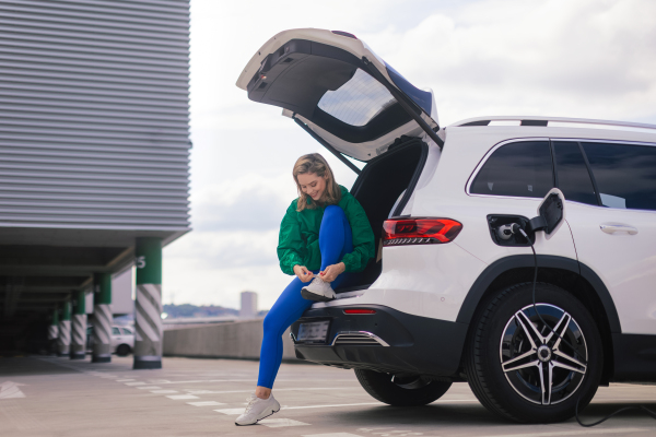 Young woman in a sportive clothes waiting for her electric car charging.