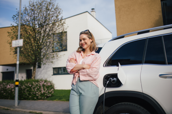 Young woman charging electric car in home, sustainable and economic transportation concept.