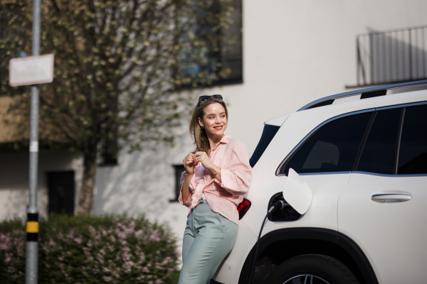 Young woman charging electric car in home, sustainable and economic transportation concept.