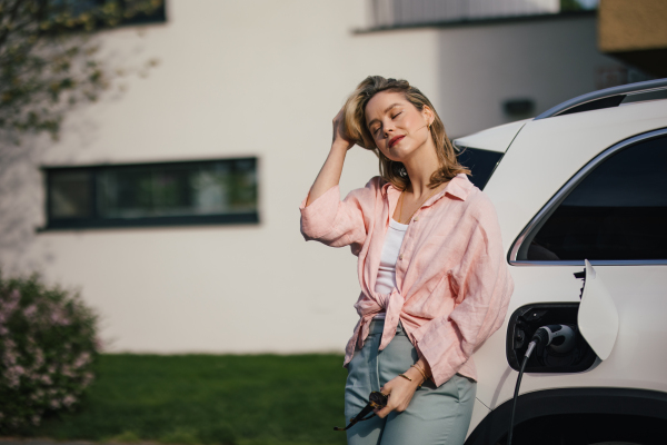 Young woman charging electric car in home, sustainable and economic transportation concept.