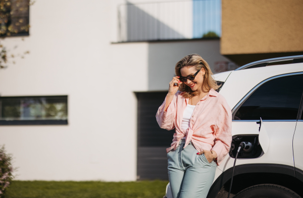 Young woman charging electric car in home, sustainable and economic transportation concept.