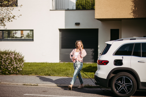 Young woman charging electric car in home, sustainable and economic transportation concept.