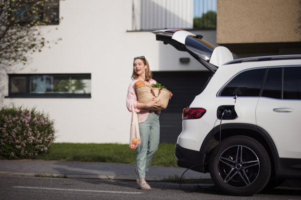 Woman coming back from a grocery store, waiting for car charging.