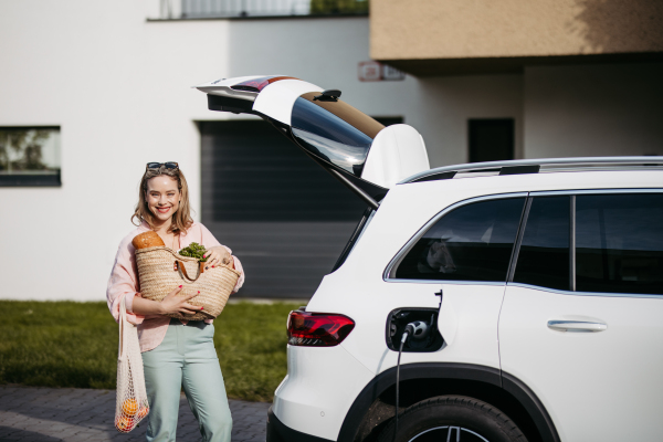 Woman coming back from a grocery store, waiting for car charging.