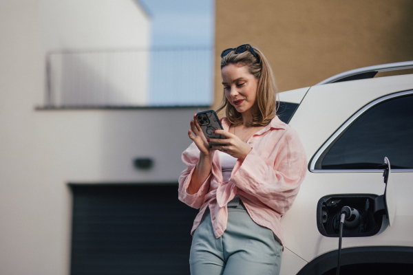 Young woman charging electric car in home, sustainable and economic transportation concept.