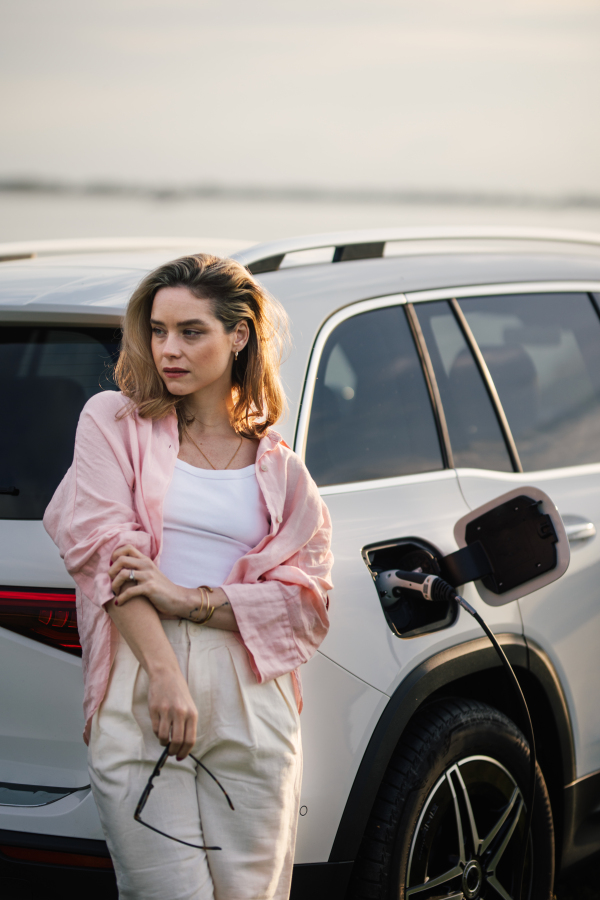 Woman waiting while charging the electric car, sustainable and economic transportation concept.