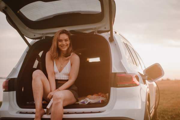 Young woman sitting in a car trunk, waiting for charging it.