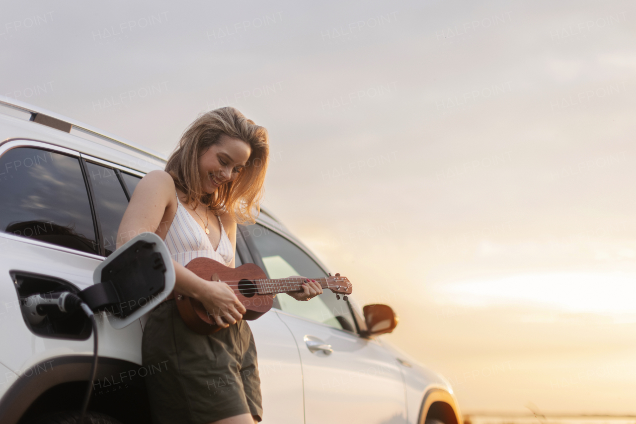 Portrait of young woman leaning on the car,playing on ukulele and enjoying summer time.