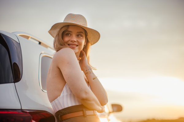 Portrait of young smiling woman standing near the car, enjoying summer time.