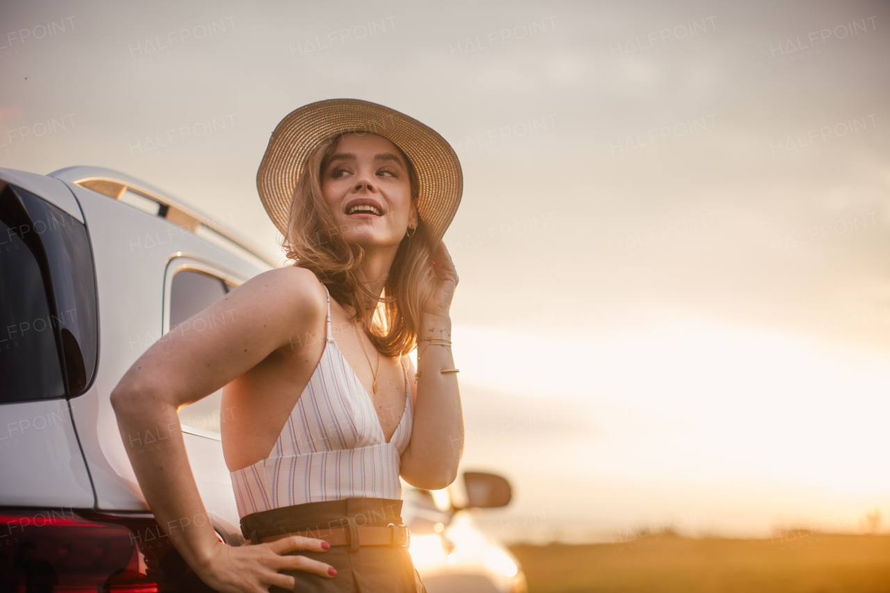 Portrait of young smiling woman standing near the car, enjoying summer time.