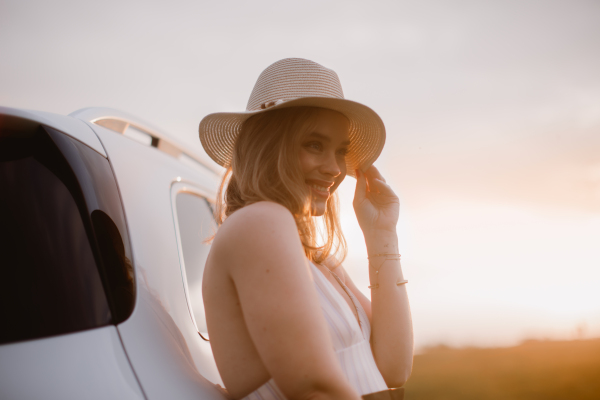 Portrait of young smiling woman standing near the car, enjoying summer time.