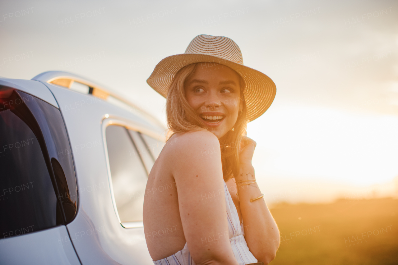 Portrait of young smiling woman standing near the car, enjoying summer time.