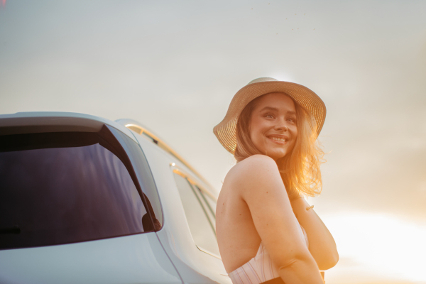 Portrait of young smiling woman standing near the car, enjoying summer time.