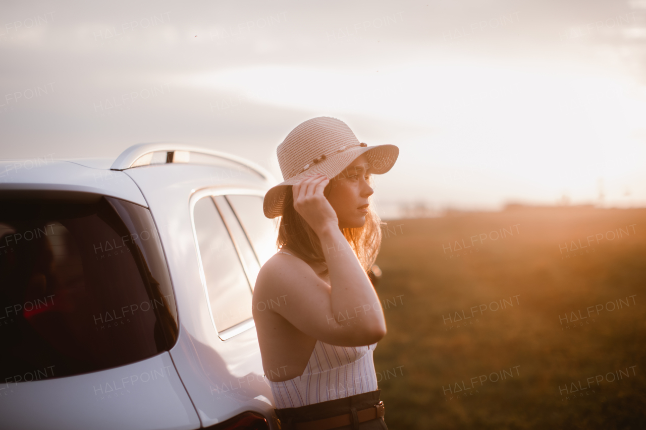 Portrait of young smiling woman standing near the car, enjoying summer time.