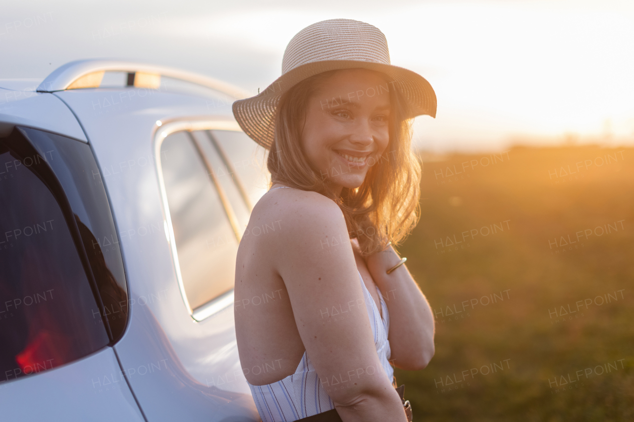 Portrait of young smiling woman standing near the car, enjoying summer time.