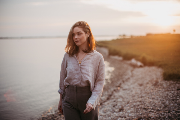 Young woman walking near the lake, enjoying summer time.