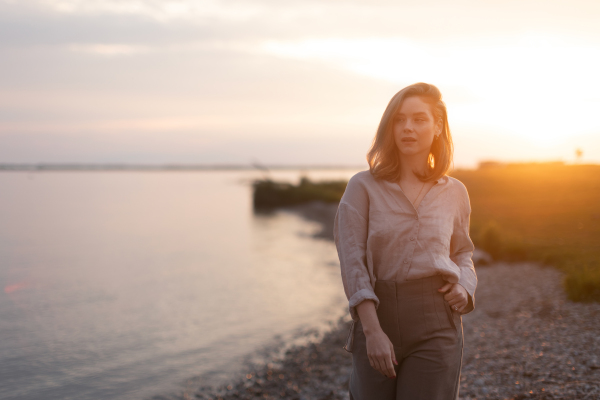 Young woman walking near the lake, enjoying summer time.