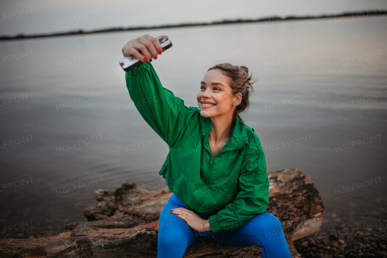 Portrait of happy woman taking selfie in sportive clothes resting near a lake.